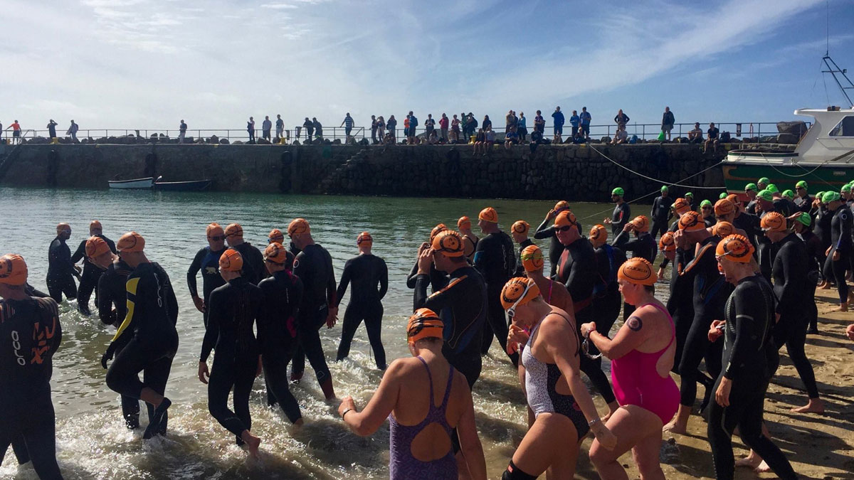 Swimmers going over pebbles as they enter the sea.